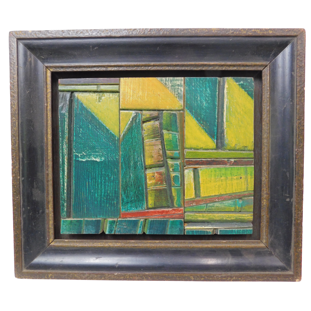 Abstract artwork with green blue and yellow hued wood pieces set in a large wooden frame on a white background